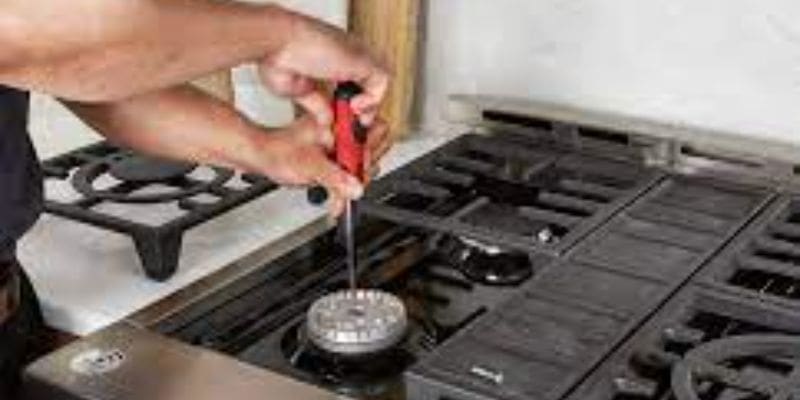 A person is using a red screwdriver to fix the burner.