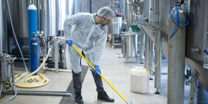 A man in white lab coat and blue gloves cleaning floor.