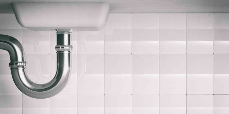 A white tiled wall with a black and silver pipe