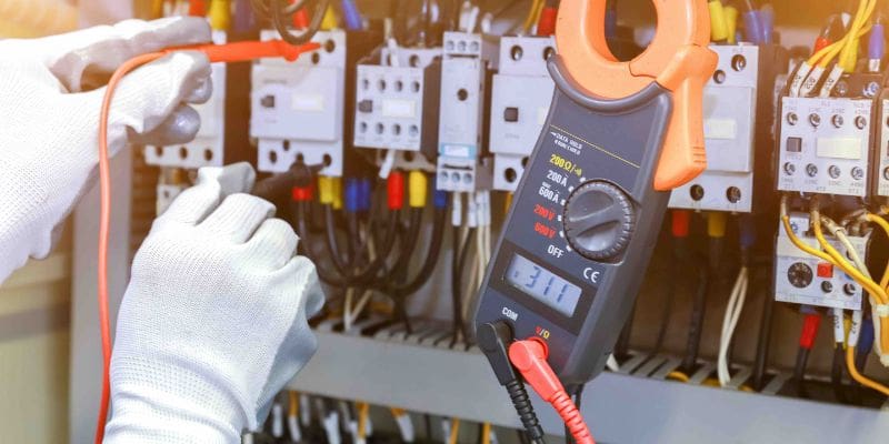 A person holding an electrical meter in front of some wires.