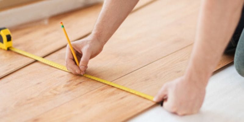 A person measuring the length of a wooden floor